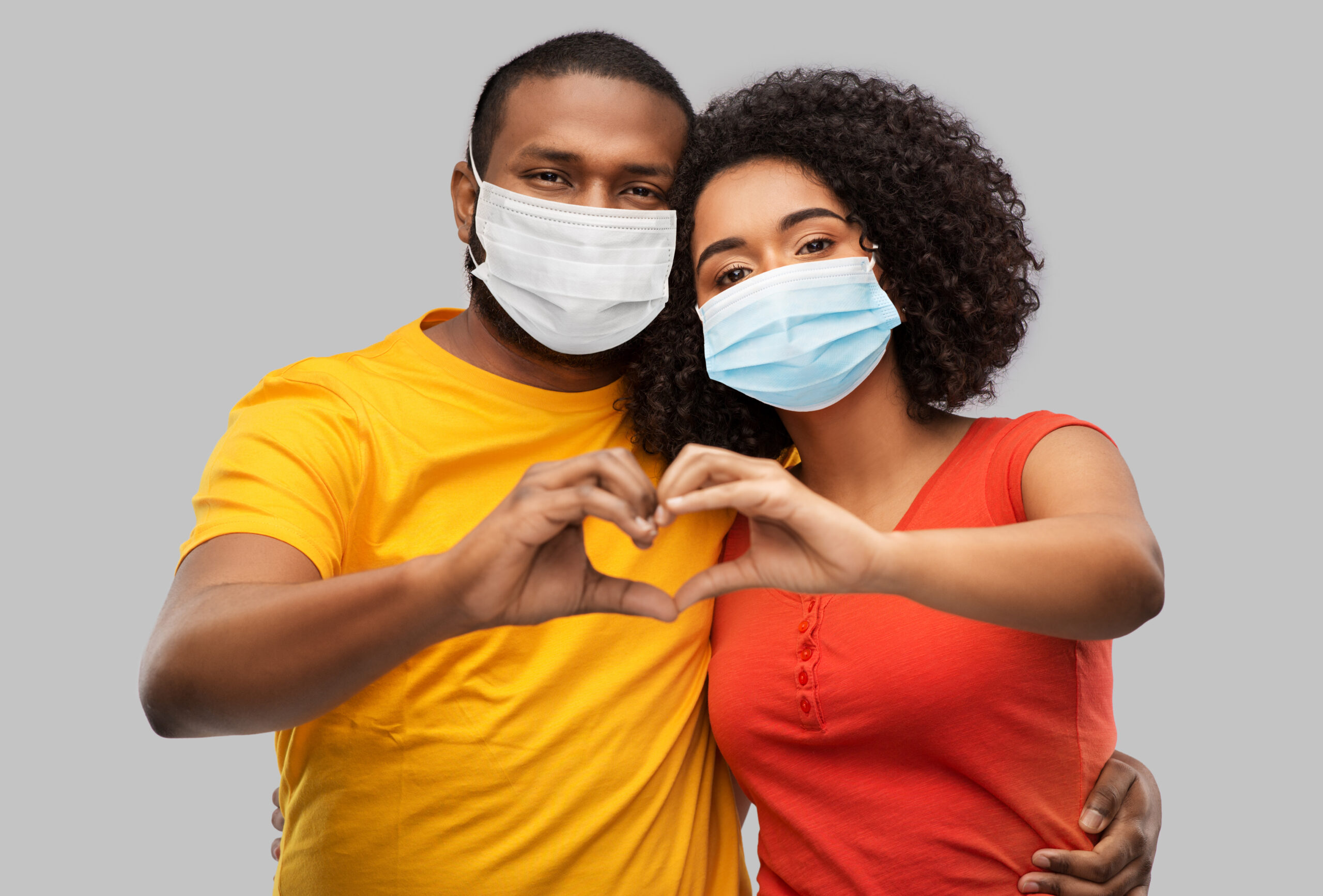 health, quarantine and pandemic concept - happy african american couple wearing protective medical masks for protection from virus making hand heart gesture over grey background